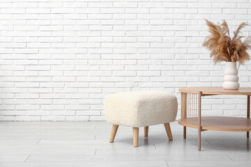 Coffee table with vase and pouf near white brick wall