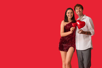 Young couple with air balloons in shape of heart on red background. Valentine's Day celebration