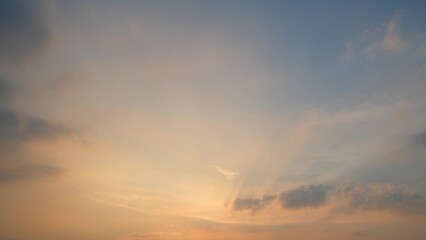 A serene sunset with a sky transitioning from soft orange near the horizon to light blue higher up. Gentle clouds scatter across, enhancing the peaceful ambiance. Sunset sky background.
