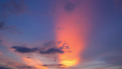 Obraz premium A breathtaking sunset with a vibrant vertical streak of pink and orange light dominating the center, contrasting against the deep blue and purple hues of the sky. Dark clouds add depth to the scene. 