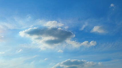 Obraz premium A serene blue sky with a scattering of fluffy white clouds. The sunlight gently illuminates the clouds, casting subtle shadows and creating a peaceful, picturesque scene. Blue sky background. 