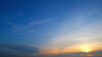 A serene sunrise with a sky that transitions from deep blue to soft yellow and orange hues. The sun is just above the horizon, casting a warm glow and gently illuminating the clouds.
