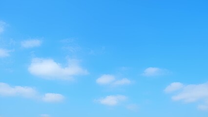 A bright blue sky adorned with a few scattered white clouds. The serene, clear sky and the soft, fluffy clouds create a peaceful and calming atmosphere, perfect for a sunny day. Nature background.
