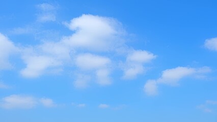 Fototapeta premium A clear blue sky dotted with a few fluffy white clouds. The bright blue expanse and scattered clouds create a serene and tranquil atmosphere, ideal for a beautiful day outdoors. Horizon background. 