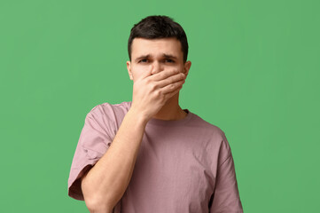 Handsome young man feeling bad smell on green background