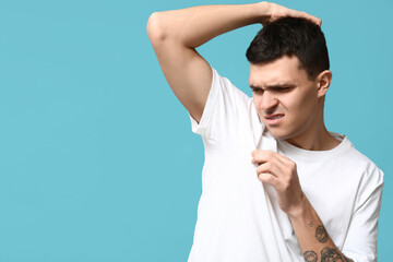 Handsome young man feeling bad smell from armpits on blue background