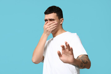 Handsome young man feeling bad smell on blue background