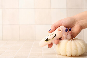 Female hand with vacuum vibrator from sex shop and bath sponge on light tile background, closeup