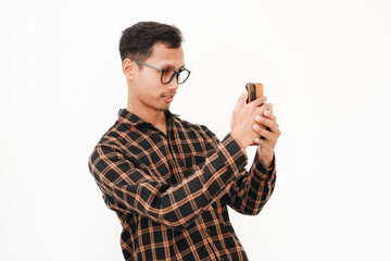 Fototapeta premium a young man wearing a flannel shirt, wearing glasses with a happy expression looking at a cellphone, videocalling, selfie. With a plain white background