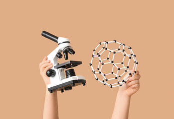 Female hands holding molecular model with microscope on beige background. Chemistry lesson concept