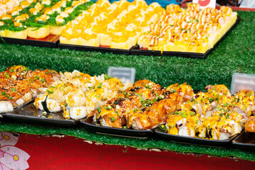 A table full of sushi with a green background. The sushi is arranged in different sections and is served on black plates