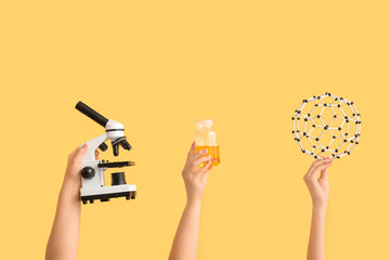 Female hands holding filled bottle with molecular model and microscope on yellow background....