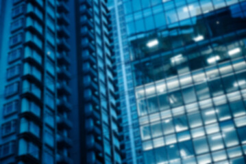 Blur background of the glass exterior of an office building located in the middle of a large city, with interior lights turning on at night.