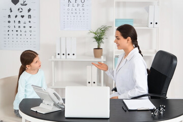 Fototapeta premium Female ophthalmologist working with little girl at table in clinic