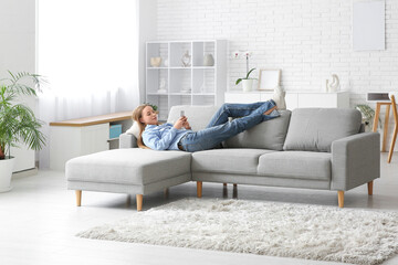 Young pretty woman lying and chatting with mobile phone on sofa in stylish living room