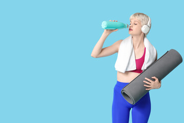 Sporty young woman with yoga mat, towel and bottle of water on blue background - Powered by Adobe