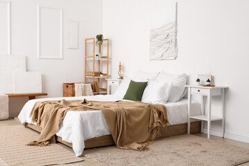 Interior of light bedroom with cozy bed and reed diffuser on bedside table