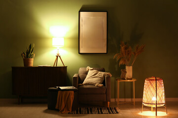 Glowing lamps on chest of drawers, armchair and picture in stylish living room