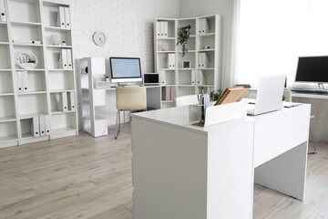 Interior of light office with modern workplaces and shelf units