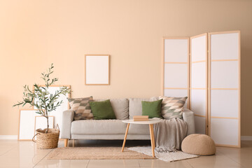 Interior of modern living room with grey sofa, coffee table, olive tree and blank frame hanging on beige wall