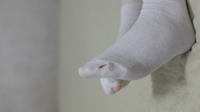 The legs of a girl lying on the bed in white, holey, torn socks. Vertical video for smartphone.
