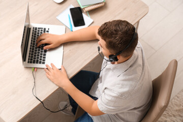 Teenage boy with laptop and headset working at home