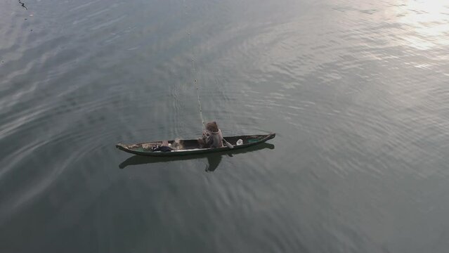 A fisherman is catching fish using a fishing net in the morning