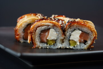Unagi maki. Ыushi roll with eel on black plate on black background
