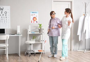 Female ophthalmologist with blind woman walking in clinic