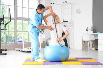 Male physiotherapist and mature woman training with stretching band in rehabilitation center