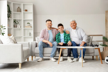 Teenage boy with his dad and grandfather sitting on sofa at home