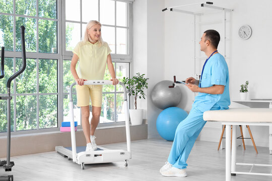 Male physiotherapist with clipboard and mature woman on treadmill in rehabilitation center - Powered by Adobe