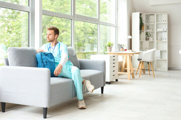 Male medical intern with backpack sitting on sofa in clinic