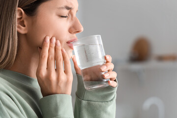 Young woman with glass of cold water suffering from tooth ache at home