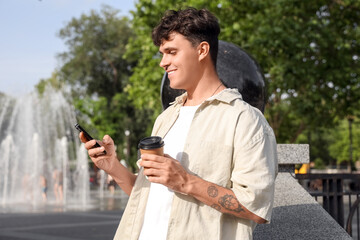 Fototapeta premium Handsome young man with cup of delicious latte and mobile phone outdoors