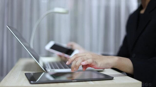 Businessman uses multiple electronic devices simultaneously holding a smartphone in hand The other hand uses a laptop. and interact with the tablet placed on the table. Technology driven environment
