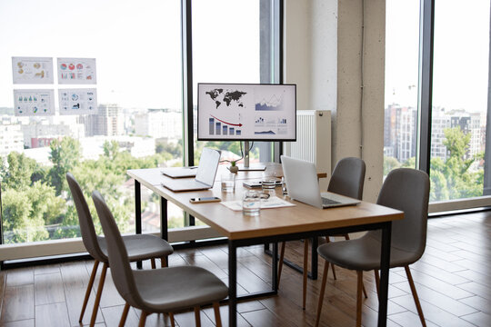 Spacious office conference room with large windows, laptops, and charts on a monitor, providing a professional business environment.