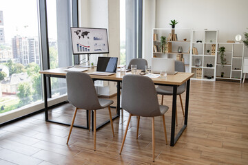Spacious and bright office conference room with a city view, featuring chairs, a desk, digital screens, and modern decor.