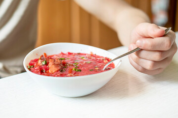 A man holding a spoon, eating soup borscht with sour cream and green onions. A tasty and healthy home-cooked meal.