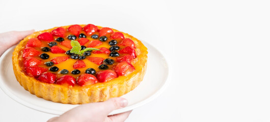 The man's hands hold a dish of mouth-watering cheesecake . Cheesecake with strawberries and blueberries on a plate. Place for text, white background.