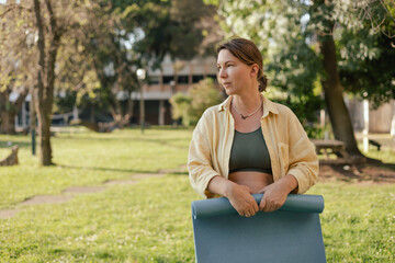 Middle aged woman with yoga mat for practicing yoga in the park. Unity with nature and self...