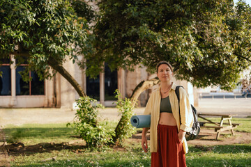 Middle aged woman with yoga mat for practicing yoga in the park. Unity with nature and self...