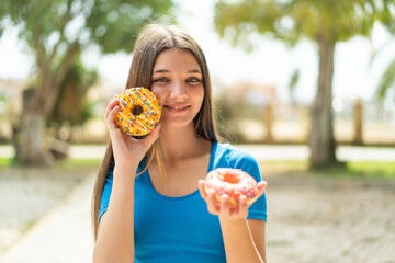 Teenager girl at outdoors holding donuts with happy expression