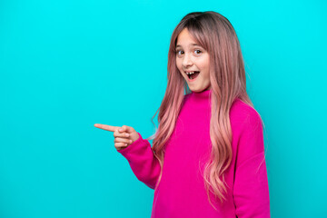 Little girl with pink hair isolated on blue background surprised and pointing finger to the side