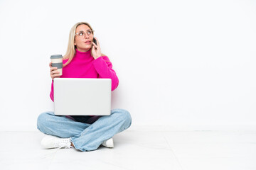 Young caucasian woman with laptop sitting on the floor holding coffee to take away and a mobile