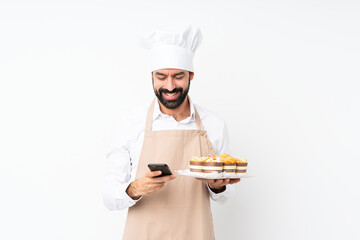 Young man holding muffin cake over isolated white background sending a message with the mobile