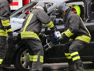 Fototapeta premium firefighters in uniform unhinging the stuck door of a crashed car after the collision using a very powerful hydraulic shear