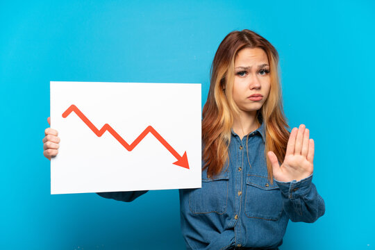 Teenager girl over isolated blue background holding a sign with a decreasing statistics arrow symbol and doing stop sign