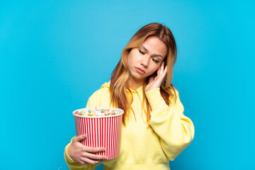 Teenager girl holding popcorns over isolated blue background with headache