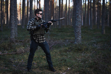 Fototapeta premium A man in sunglasses in tactical gear with an assault rifle in his hands plays airsoft in the forest in the summer.